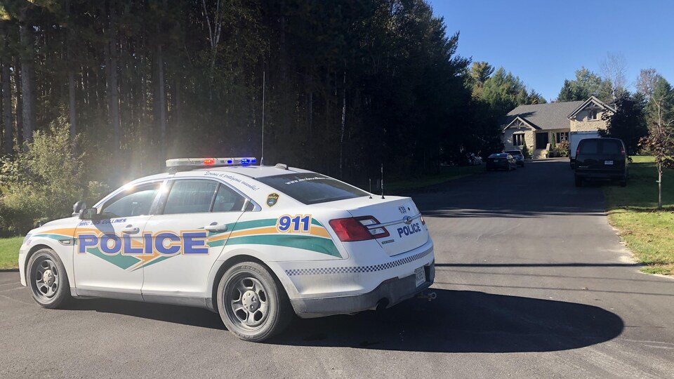 Une voiture de police de la Sécurité publique de la MRC des Collines-de-l'Outaouais stationnée devant une maison.