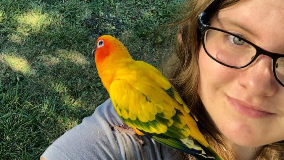 Une femme se prend en égoportrait avec un perroquet jaune sur son épaule.
