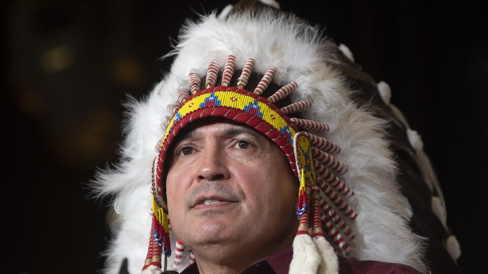 Gros plan sur le visage de Perry Bellegarde, qui porte la coiffe traditionnelle à plumes.