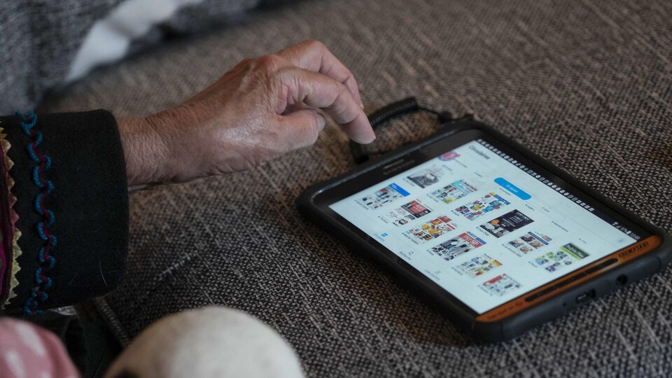La main d'une dame âgée sur une tablette dont l'écran d'accueil montre un assortiment de circulaires.