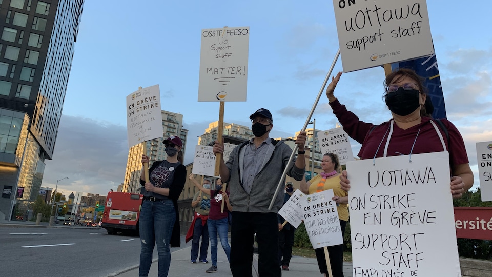 Des employés de l'Université d'Ottawa brandissent des pancartes dans les rues d'Ottawa.