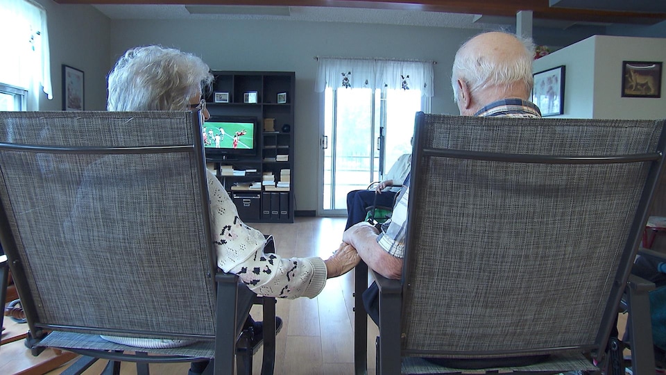 Un couple âgé se tenant par la main en regardant le soccer à la télévision.