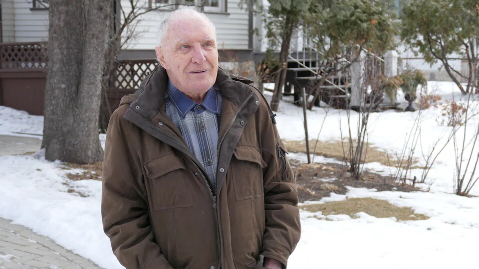 Peter Hanlon, les mains dans les poches de son manteau, dehors devant une maison.