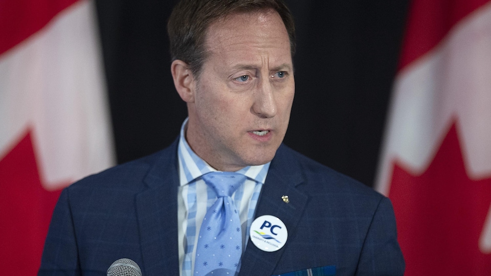 M. MacKay s'adressant à des partisans conservateurs à Halifax, avec en arrière-plan, deux drapeaux canadiens.