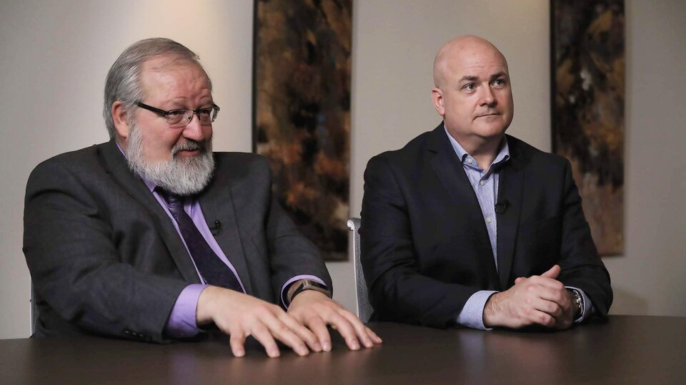 Deux hommes assis à une table répondent à des questions.