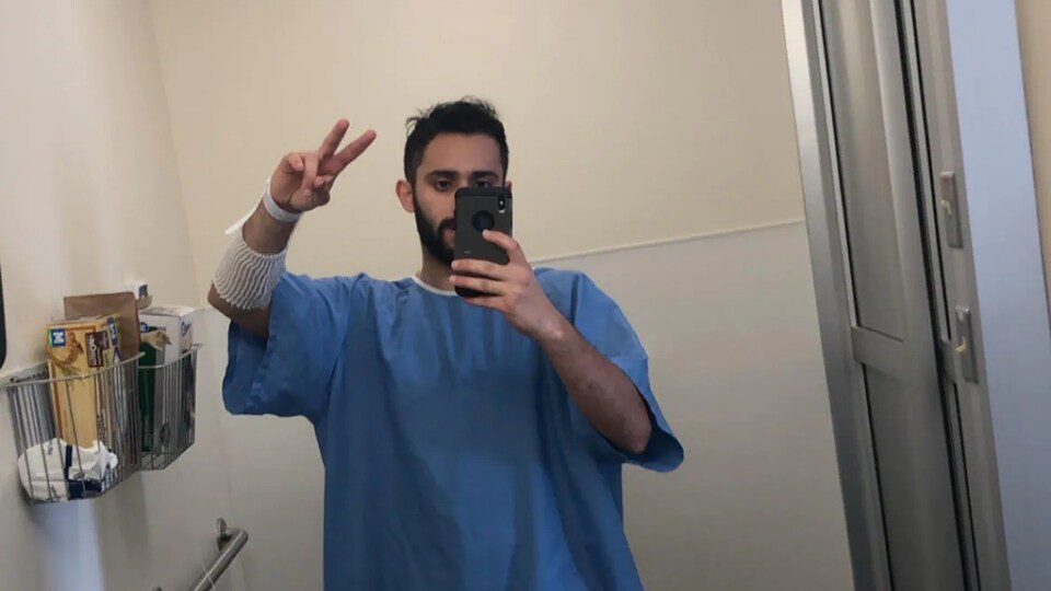 Peter Soliman prend un égoportrait devant le miroir du salle de bain d'hôpital, vêtu d'une chemise d'hôpital.