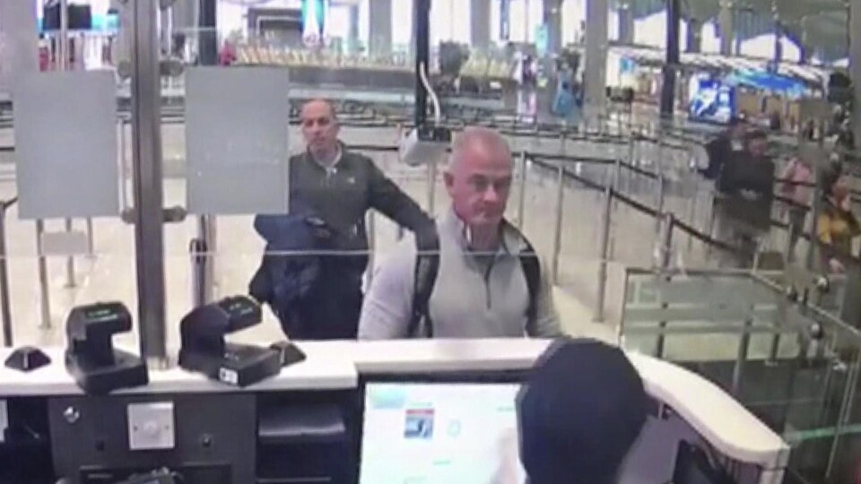 Deux hommes attendent devant un guichet des douanes dans un aéroport.