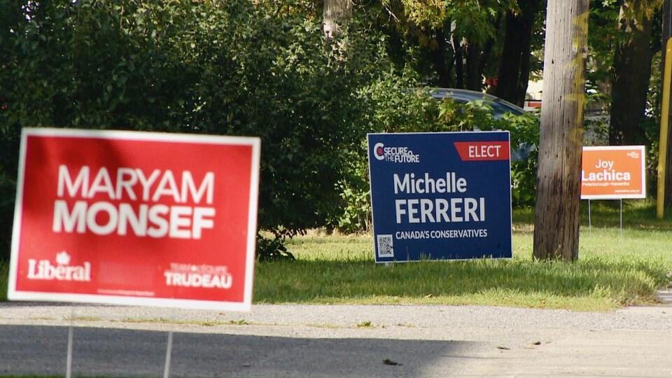 Trois affiches électorales dans une rue; une rouge, avec le nom de Maryam Monsef, une bleue, avec le nom de Michelle Ferreri, une orange avec le nom de Joy Lachica.