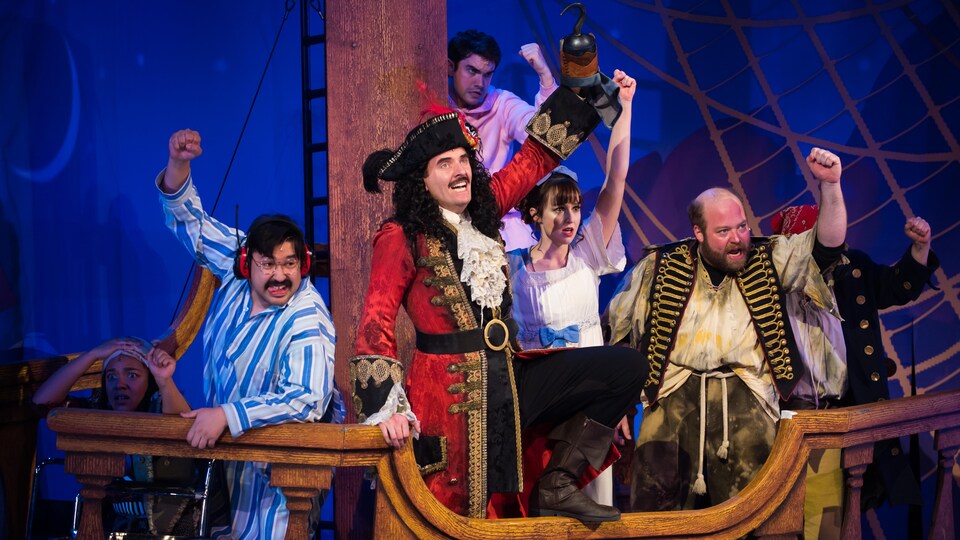 Sept personnages, dont un pirate, sur scène à bord d'un bateau.