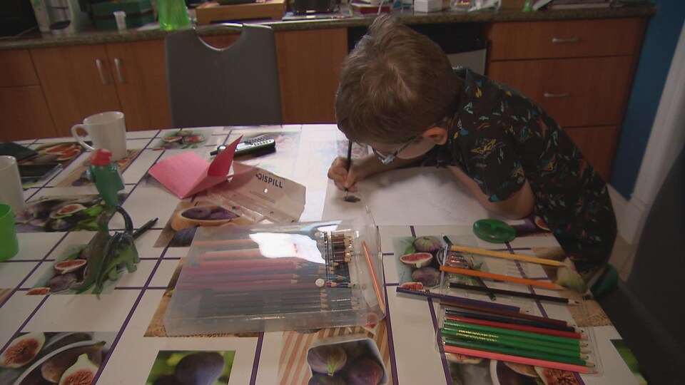 Le petit Charles, âgé de 7 ans, dessine à une table.