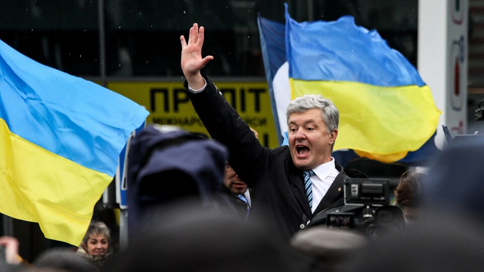 Petro Porochenko lève la main devant une foule. Près de lui flottent des drapeaux ukrainiens.