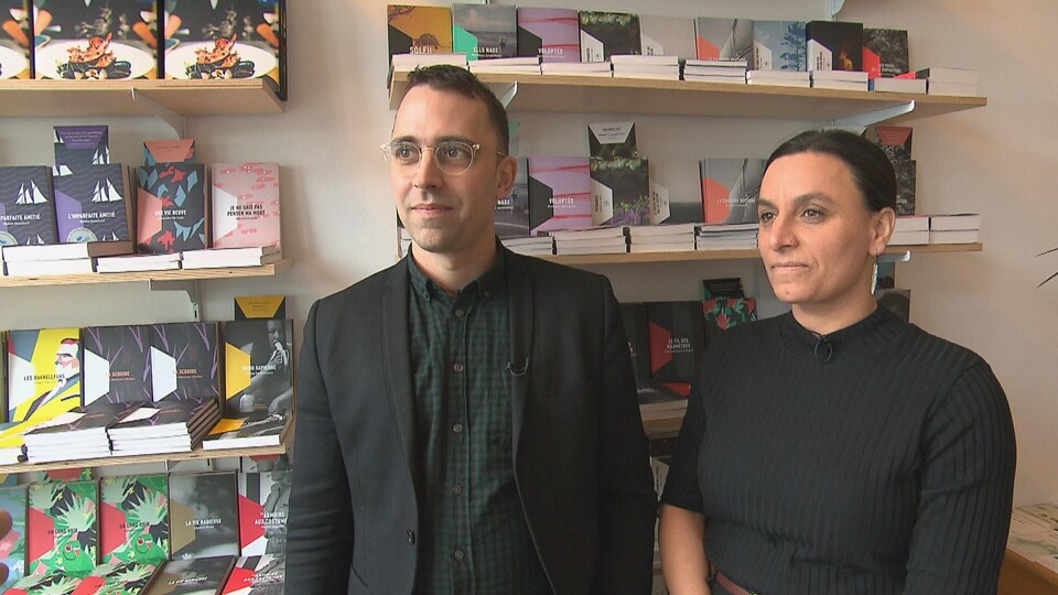 Un homme avec des lunettes et une femme sourient. Derrière eux, des livres de la maison d'édition.