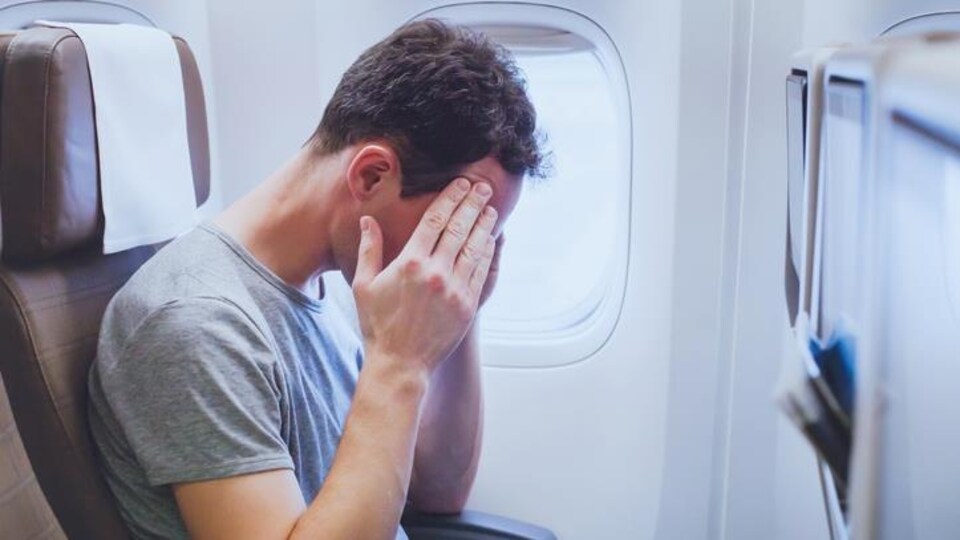 Un homme assis la tête entre les mains dans un avion.