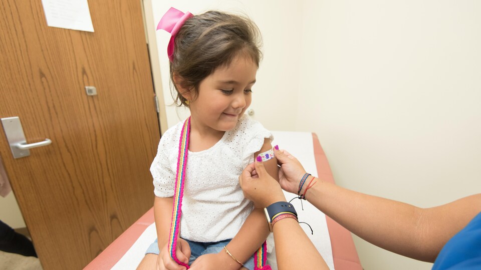 Une infirmière applique un bandage sur le bras d'une petite fille qui vient d'être vaccinée.