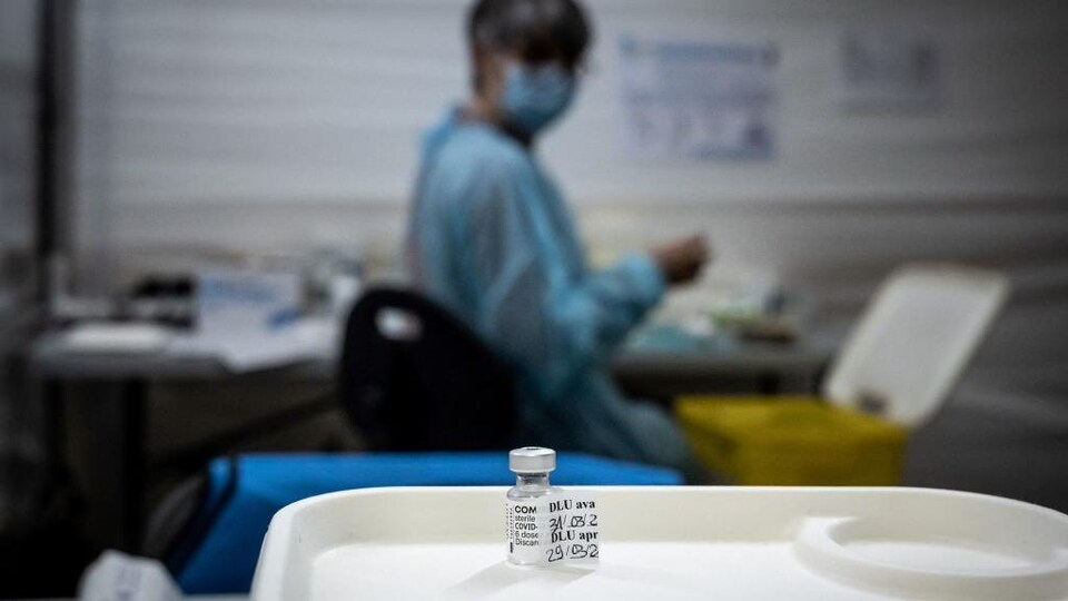 Une fiole contenant le vaccin de Pfizer-BioNTech photographiée dans la clinique de vaccination avec une infirmière en arrière-plan