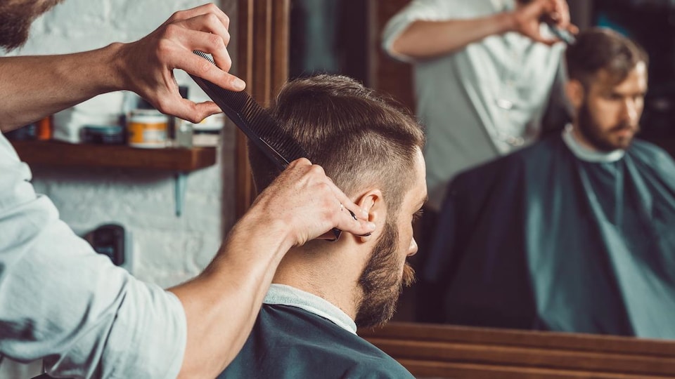Un homme se fait couper les cheveux par un coiffeur.