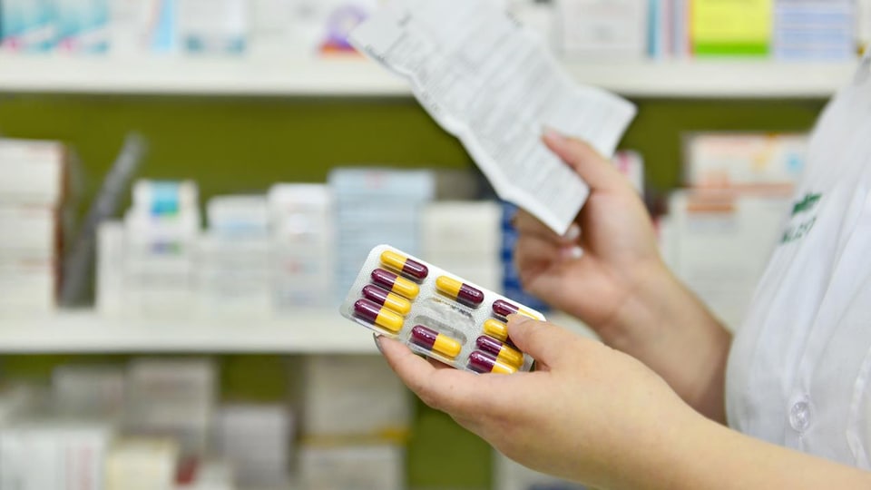 Une pharmacienne tient une ordonnance dans une main et une plaquette de médicaments dans l'autre.
