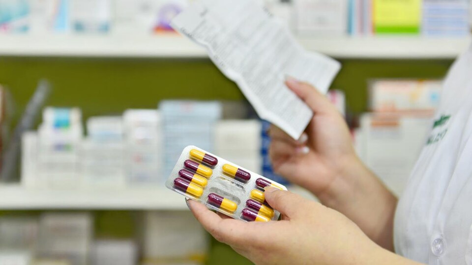 Une pharmacienne tient une ordonnance dans une main et une plaquette de médicaments dans l'autre. 