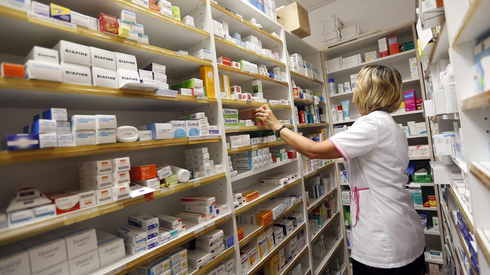 Une pharmacienne recherche un médicament parmi les nombreux produits placés sur des étagères de son magasin.