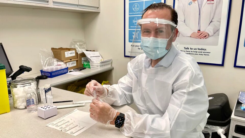 Le pharmacien, portant le masque et une visière, tient dans ses mains des outils pour offrir le dépistage.