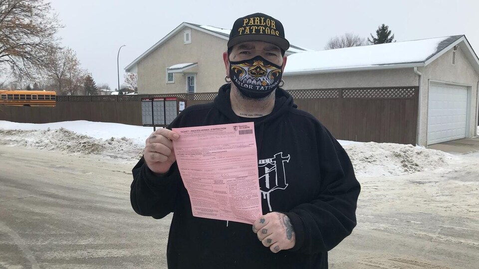 Phil McLellan avec des tatouages plein les mains, tient une feuille de papier rose.