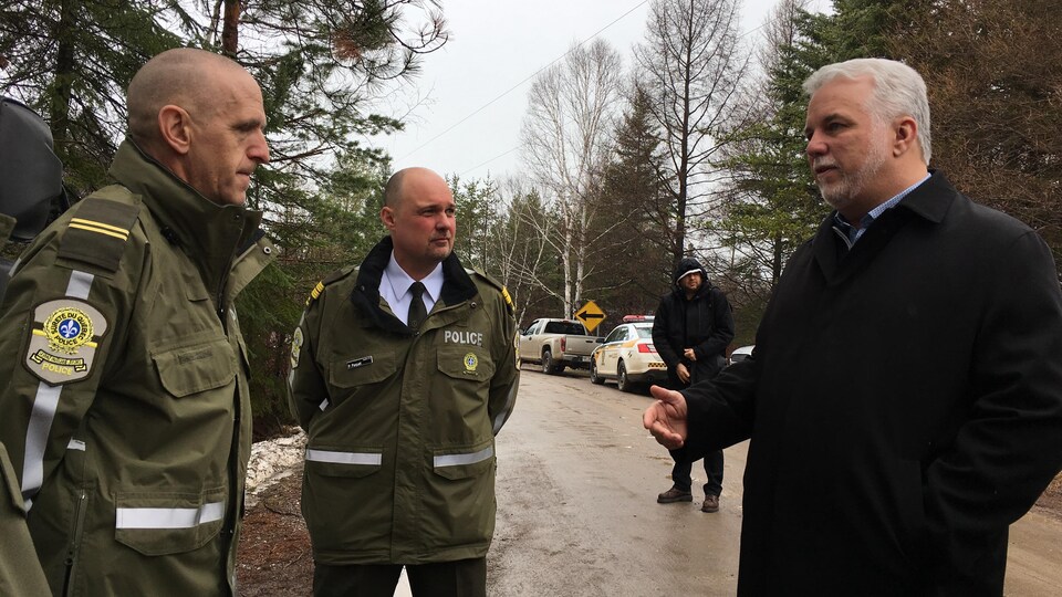 Philippe Couillard discute avec deux agents de la Sûreté du Québec.