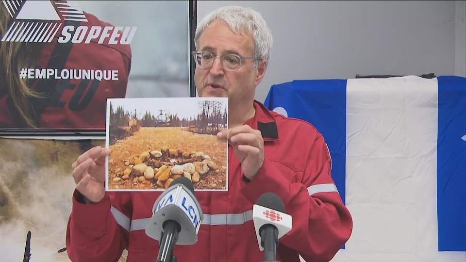 Pierre Dufour tient une photo dans ses mains et montre le feu de camp qui aurait été mal éteint la semaine dernière.