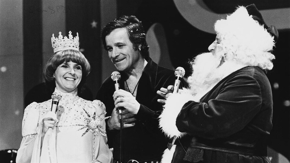 Sur cette photo en noir et blanc, l'homme tient un micro avec une femme et le père Noël à ses côtés.