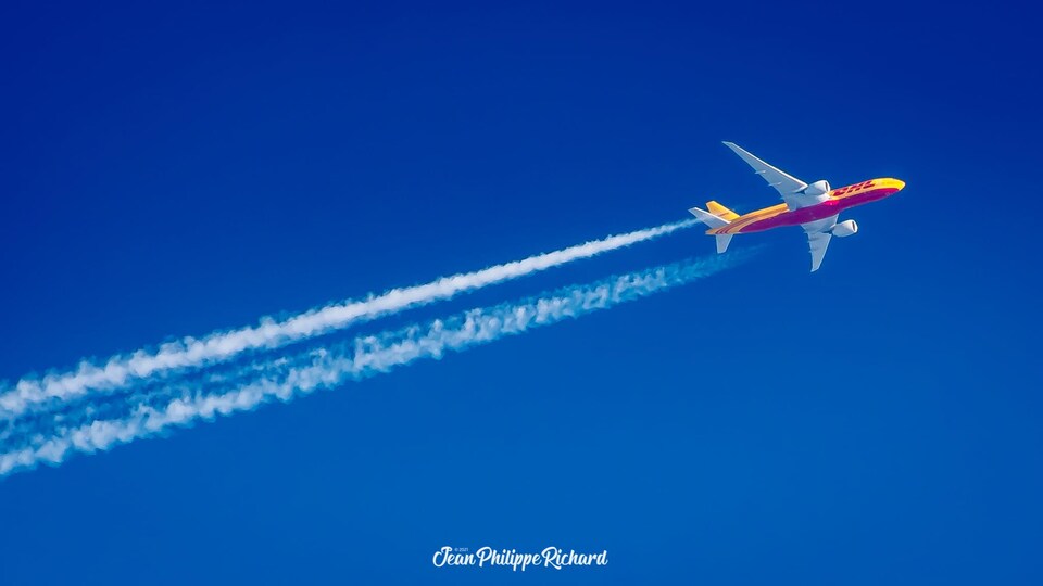 Un avion jaune et mauve dans le ciel bleu clair laisse une traînée de fumée blanche derrière lui.