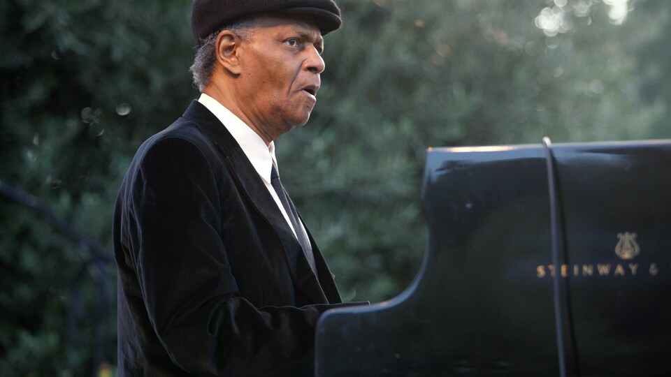 L'homme porte une casquette et joue du piano.