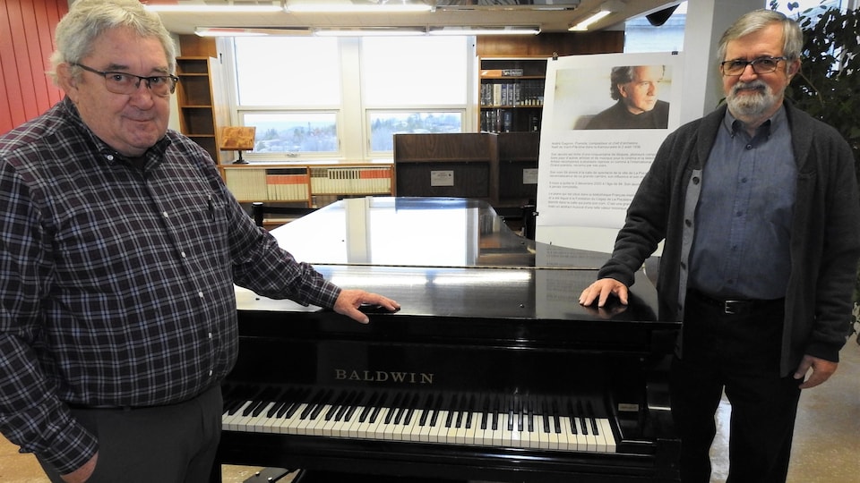 Deux hommes se trouvent de part et d'autre d'un piano à queue Baldwin ayant appartenu au musicien André Gagnon. 