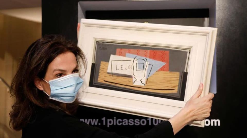 Une femme portant un masque hygiénique tient la toile de Picasso entre ses mains.