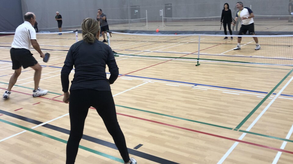 Deux personnes de chaque côté du filet se font des passes dans un gymnase.