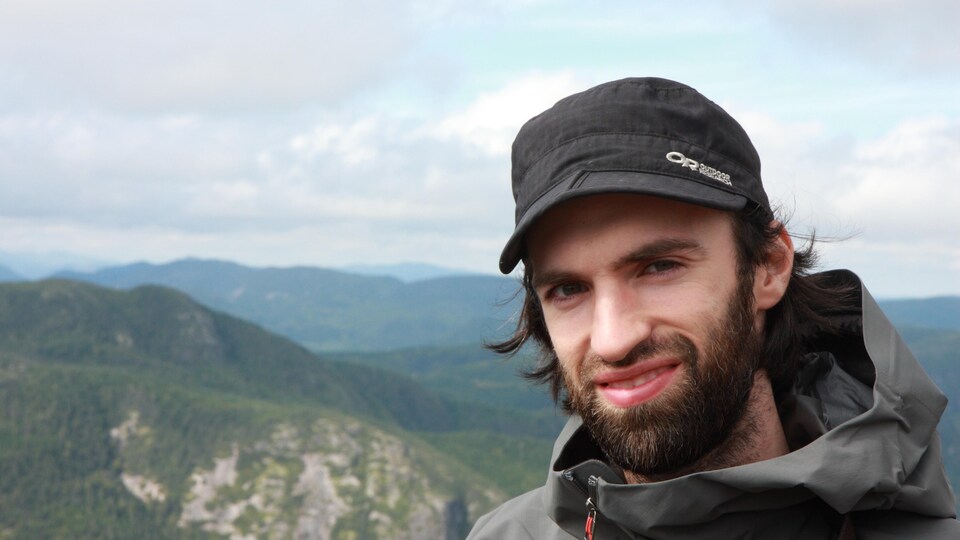 Pier-Olivier Boudreault sourit pour la photo au sommet d'une montagne devant un paysage montagneux.
