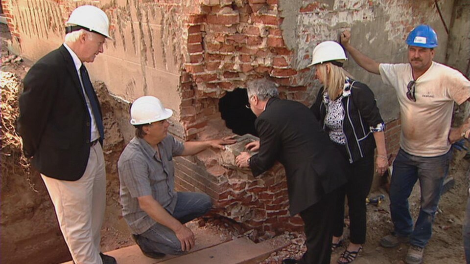 Un curé lit un inscription en latin sur la pierre angulaire trouvée sur le chantier de démolition