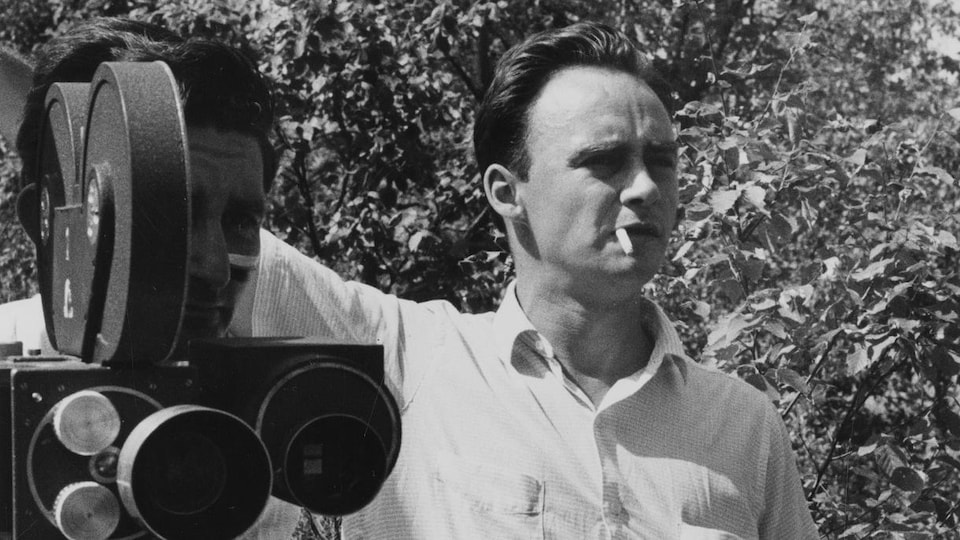 Pierre Gauvreau, cigarette à la bouche, lors d'un tournage extérieur à l'Île
Perrot. Il se tient aux côté d'un caméraman.