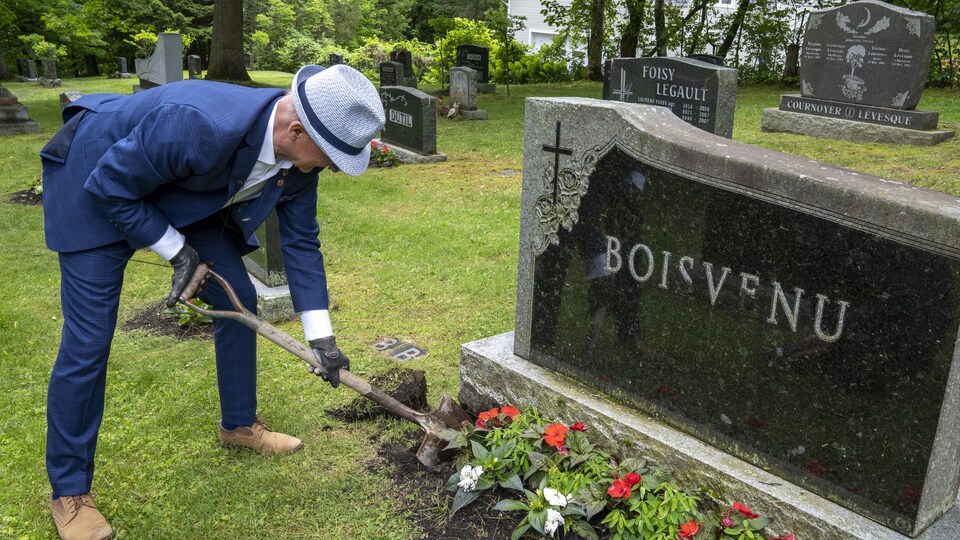 M. Boisvenu creuse un trou devant une pierre tombale pour y planter des fleurs.