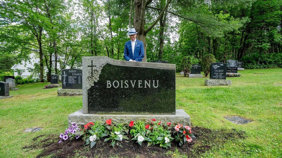 Pierre-Hugues Boisvenu se recueille sur la tombe de ses filles. Sur le devant de la pierre tombale est inscrit Boisvenu. La pierre est entourée de fleurs. 