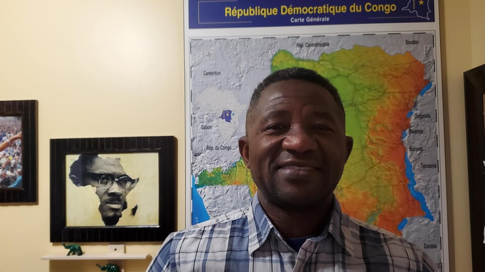 Pierre Kasongo regardant la caméra devant une carte de la RDC et un portrait de l'ancien premier ministre congolais Patrice Émery Lumumba.