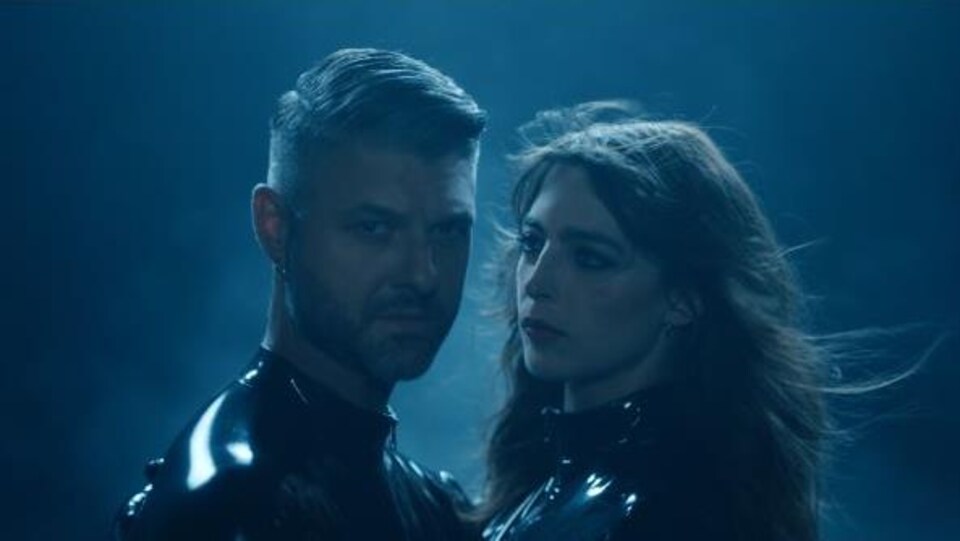 Un homme et une femme se font face dans un extrait de vidéoclip teinté de lumière bleue. 