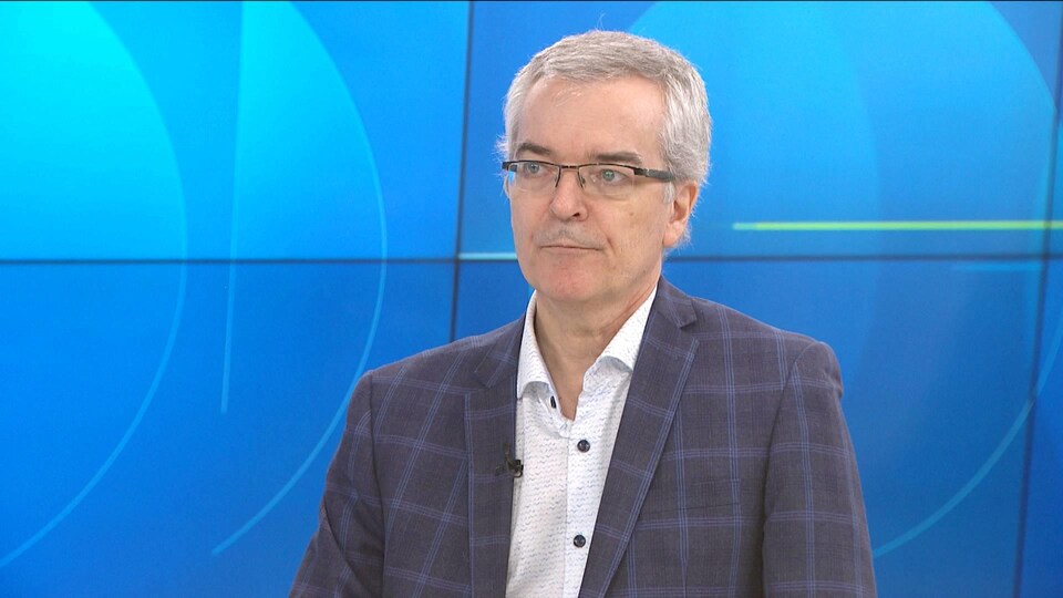 Pierre-Marcel Desjardins en entrevue sur un plateau de télévision. Il est debout devant un fond bleu.