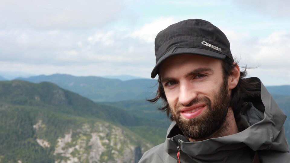 Un homme sourit devant un paysage montagneux.