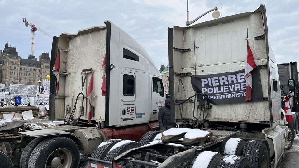 Une banderole affichée derrière un camion, où l'on peut lire : « Pierre Polievre pour premier ministre » (en anglais).