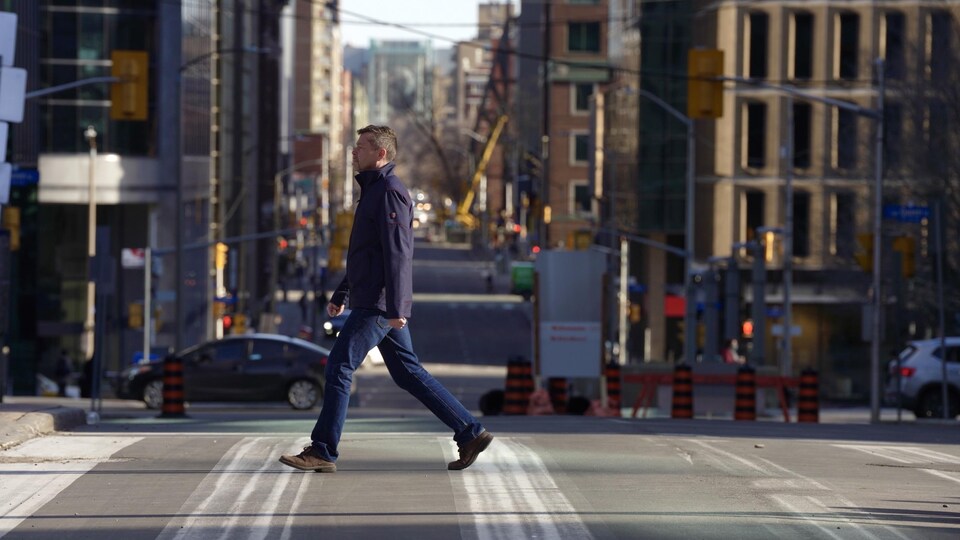 Un piéton traverse une rue du centre-ville d'Ottawa, le 21 mars 2022. C'est une journée ensoleillée. Il n'y a pas de neige au sol.