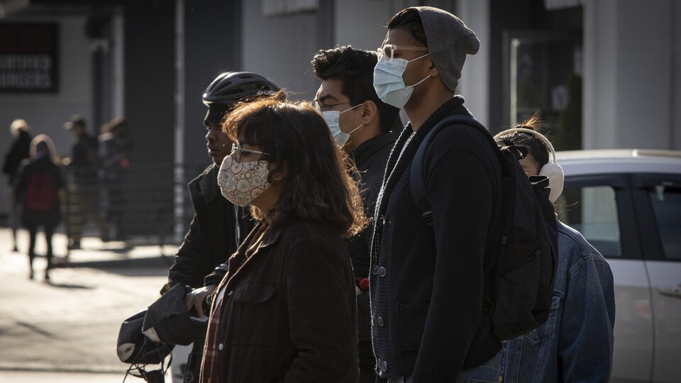 Des piétons, dont la plupart portent des masques, attendent à une intersection à Toronto.