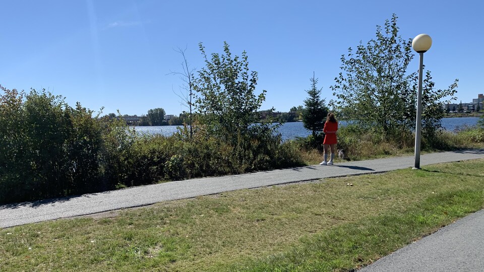 Une femme lit un livre debout devant le lac Osisko. Son chien en laisse renifle le gazon.