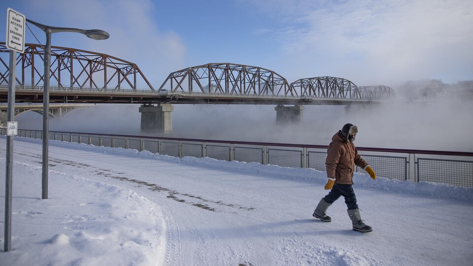 Un piéton marche le long de la rivière au centre-ville de Saskatoon, en Saskatchewan, lors d'une vague de froid le 25 janvier 2021.