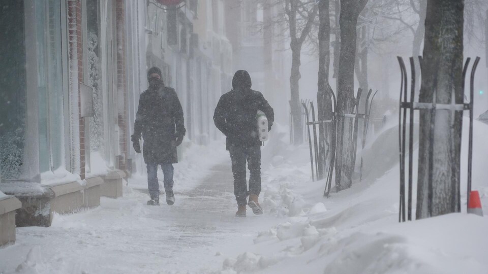 Deux passants marchent dans la tempête au centre-ville de Rimouski.