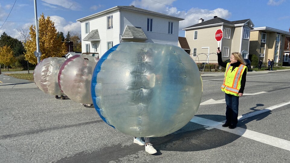 Trois enfants, vêtus de bulles gonflables, traversent une intersection.