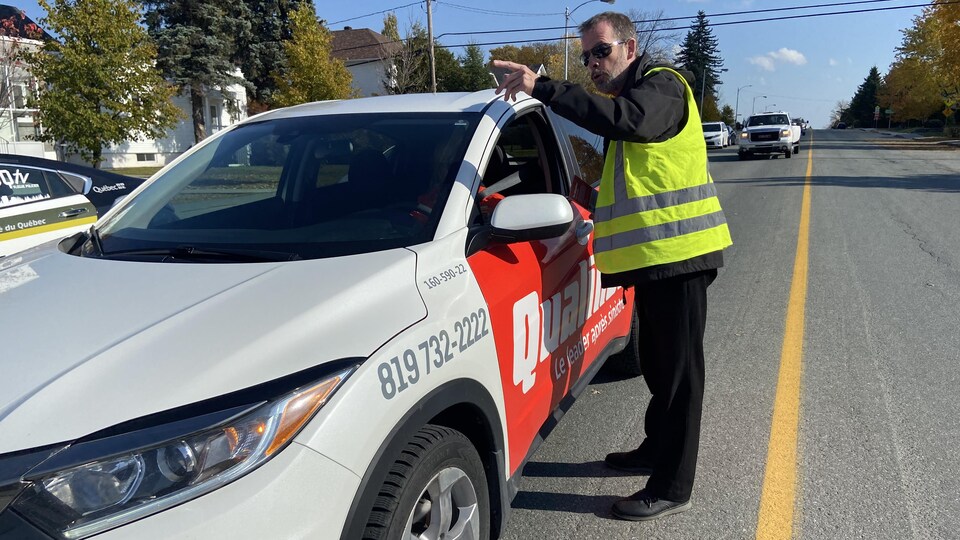 Mario Brunet remet un dépliant à un automobiliste en pointant quelque chose.